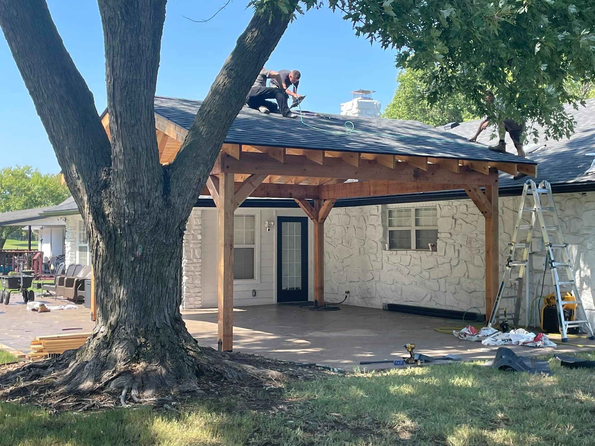 Construction of a wooden patio cover attached to a white brick house, a worker on the roof.