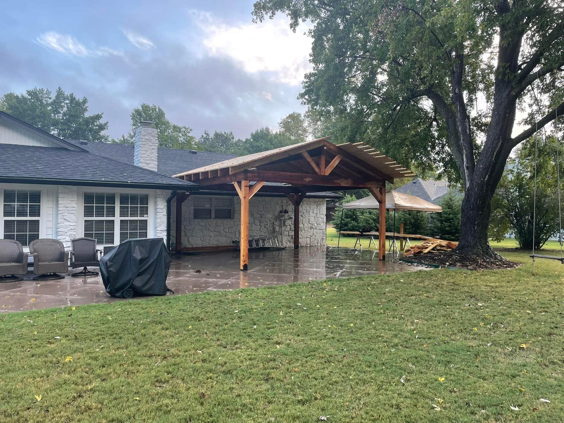 Patio with a wooden pergola, brick columns, and a grassy yard; cloudy sky overhead.