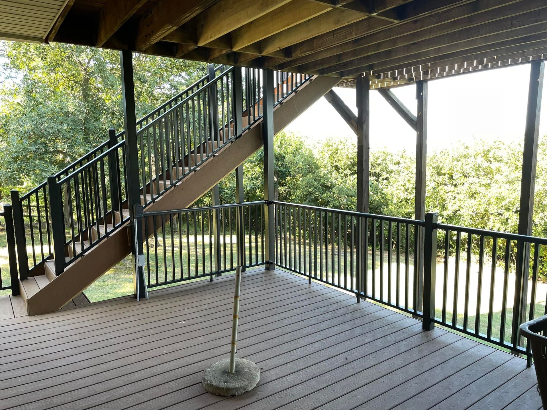 Covered deck with stairs, black railings, and a view of trees.