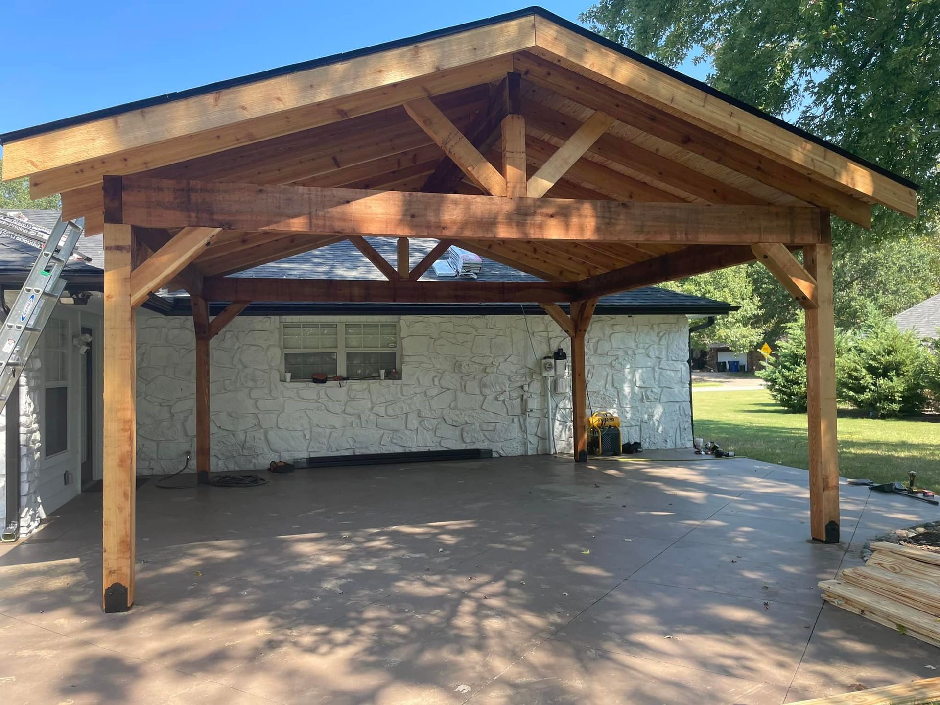 Wooden carport extension attached to a white stucco building with a concrete patio.