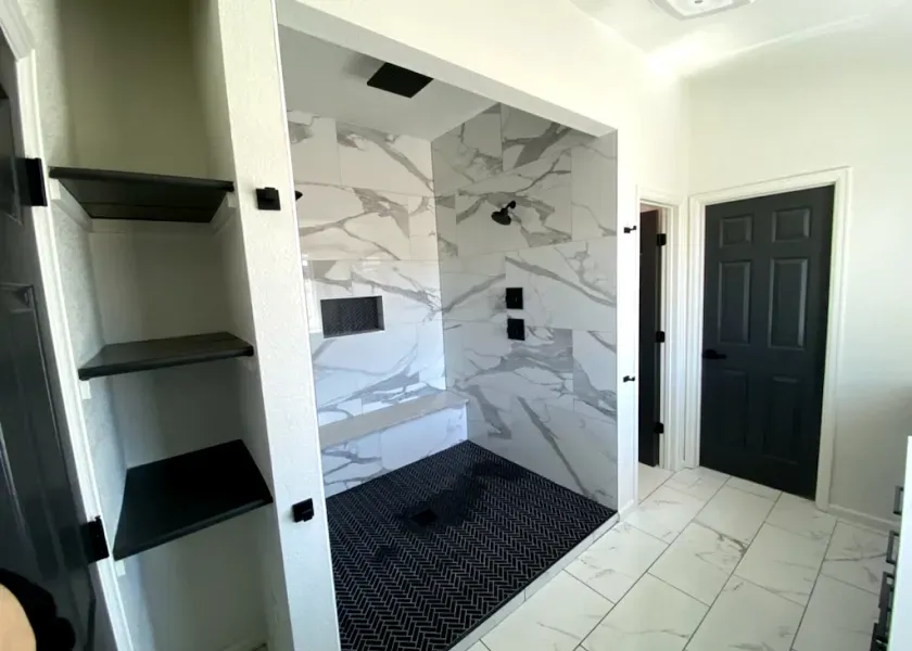 A bathroom with a walk in shower and a black door.