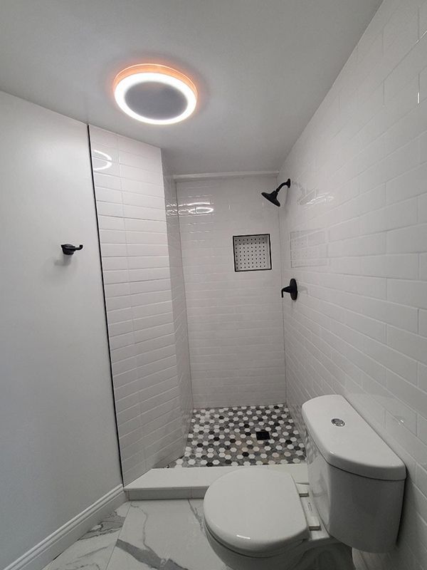 A bathroom with a toilet , shower and a light on the ceiling.