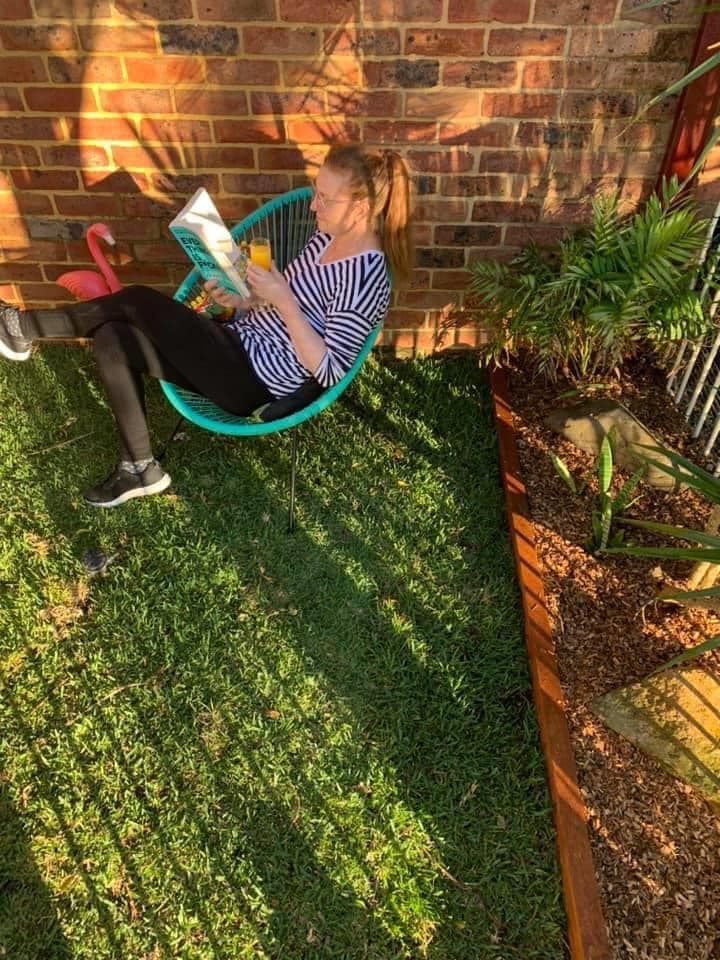 A Woman is Sitting in a Chair in the Grass Reading a Book | Central Coast, NSW | Budget Lawns Plus