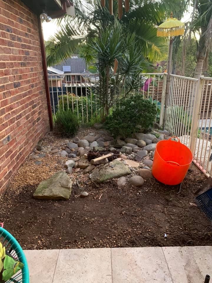 A Red Bucket is Sitting in the Dirt in Front of a Brick Wall | Central Coast, NSW | Budget Lawns Plus