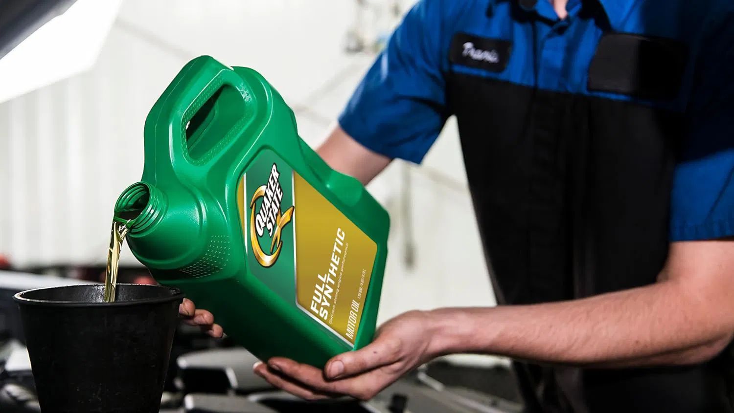 Mechanic pouring green oil container into a black funnel during an oil change.