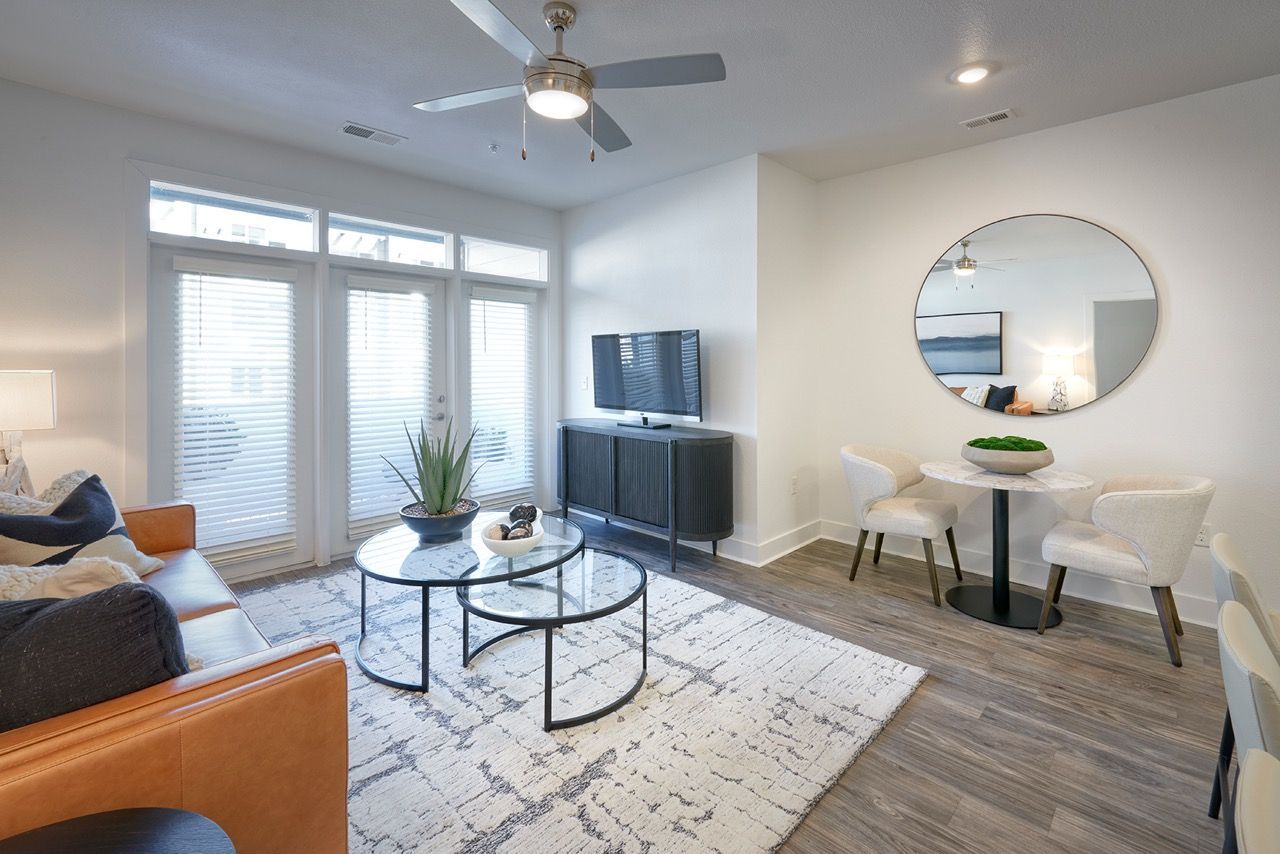 Living room in a modern apartment with a sofa, glass coffee tables, TV, and a round wall mirror.