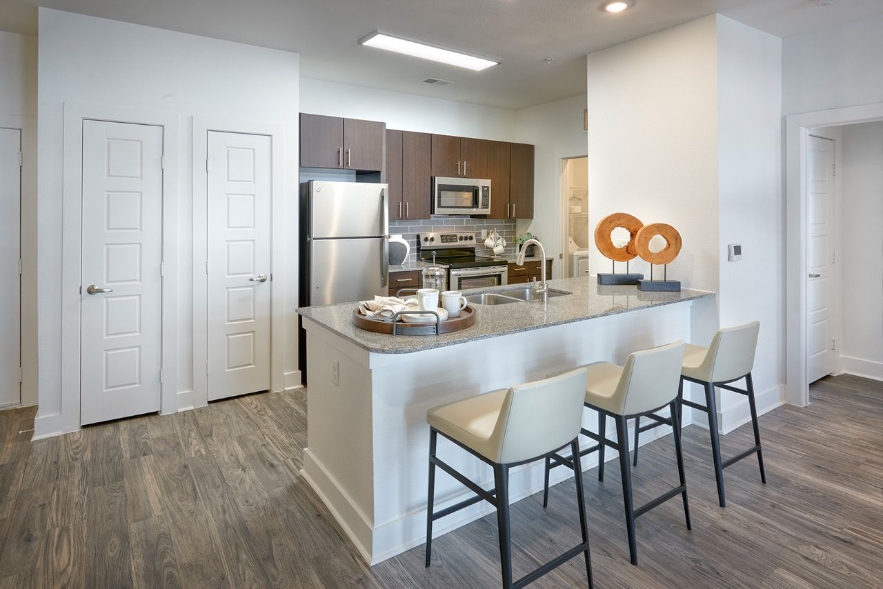 Modern kitchen with an island, granite countertops, stainless steel appliances, and three bar stools.