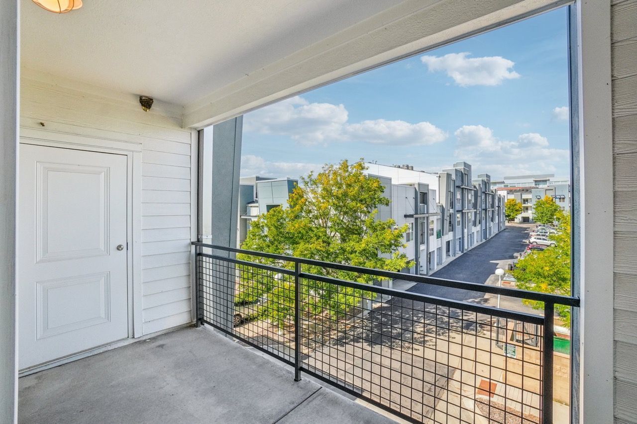 Balcony with black metal railing, concrete floor, overlooking modern apartment buildings and trees.