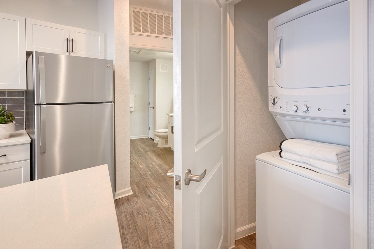 Open kitchen with white cabinets, stainless steel refrigerator, and a stacked washer/dryer in a closet.