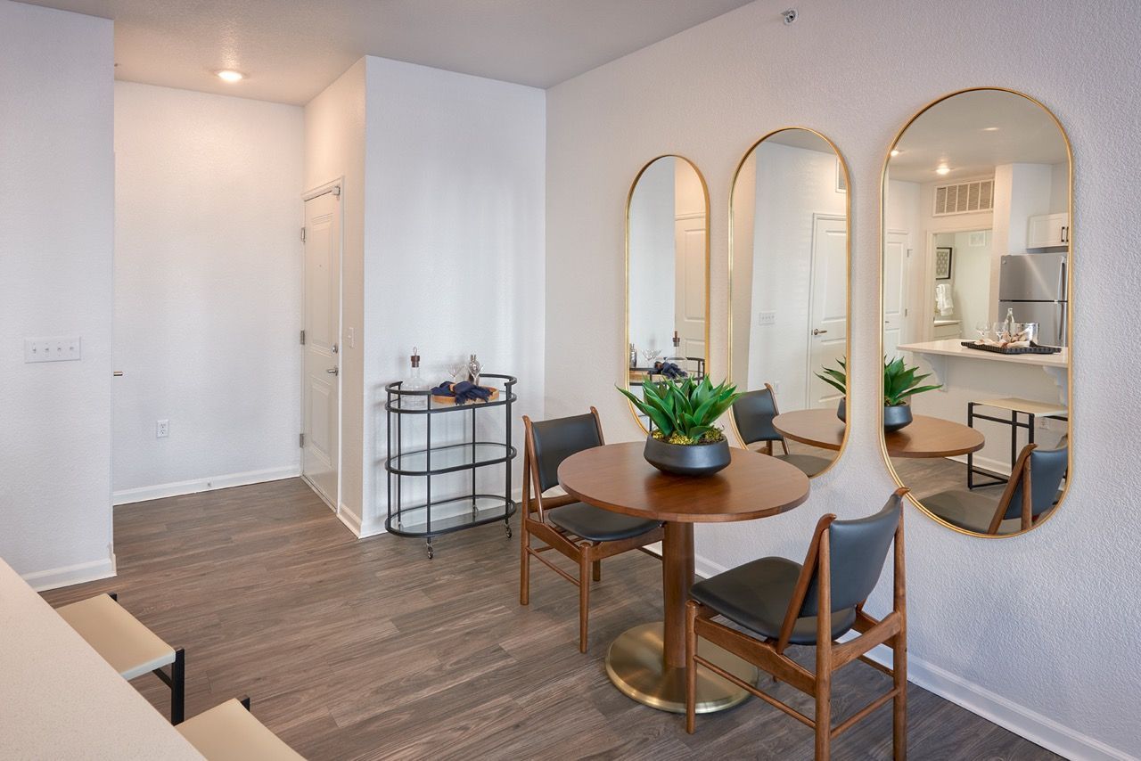 Interior dining area in an apartment with a round table, chairs, and three arched mirrors on the wall.