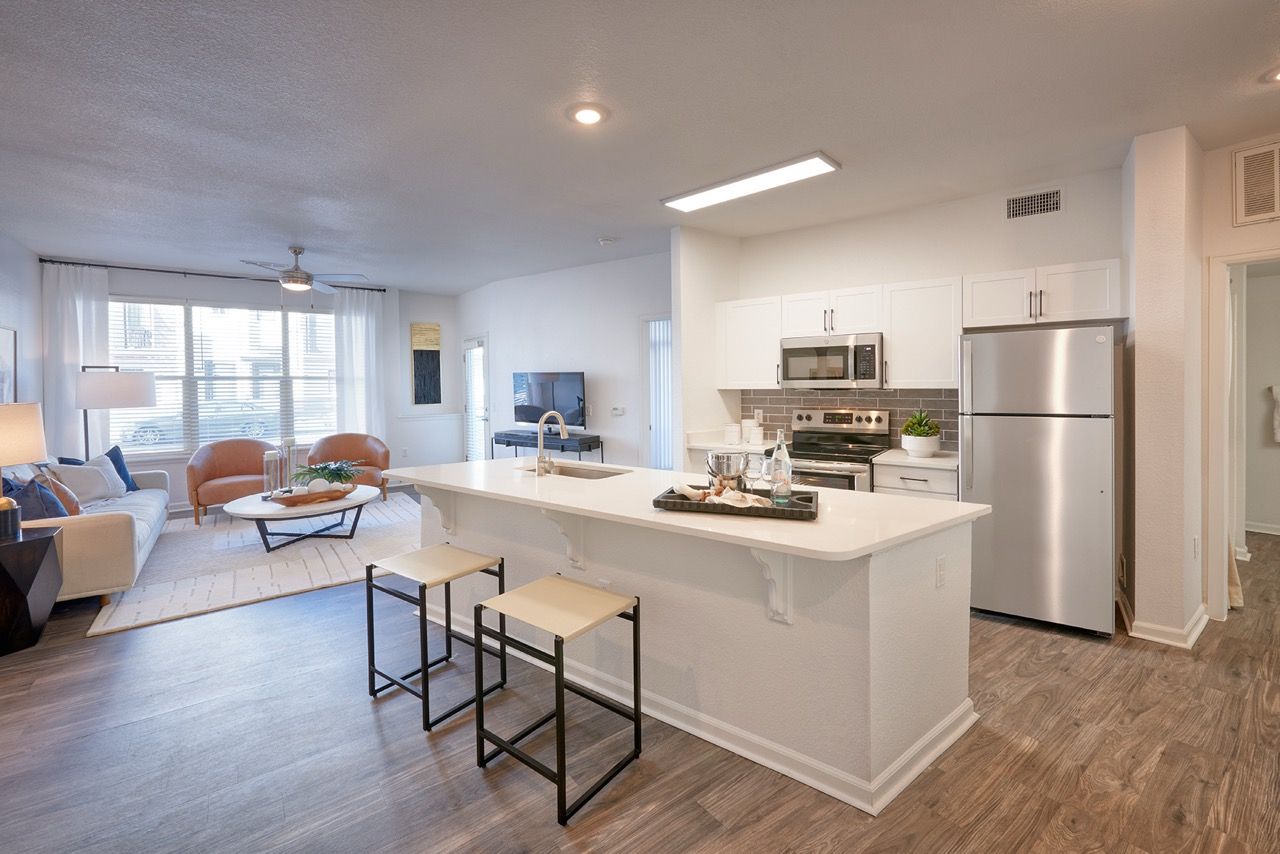 Open-concept kitchen and living area in a modern apartment with white cabinets and stainless appliances.