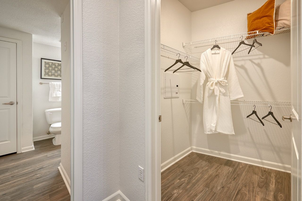 Walk-in closet with wire shelving, multiple hangers, and a robe; bathroom doorway visible.