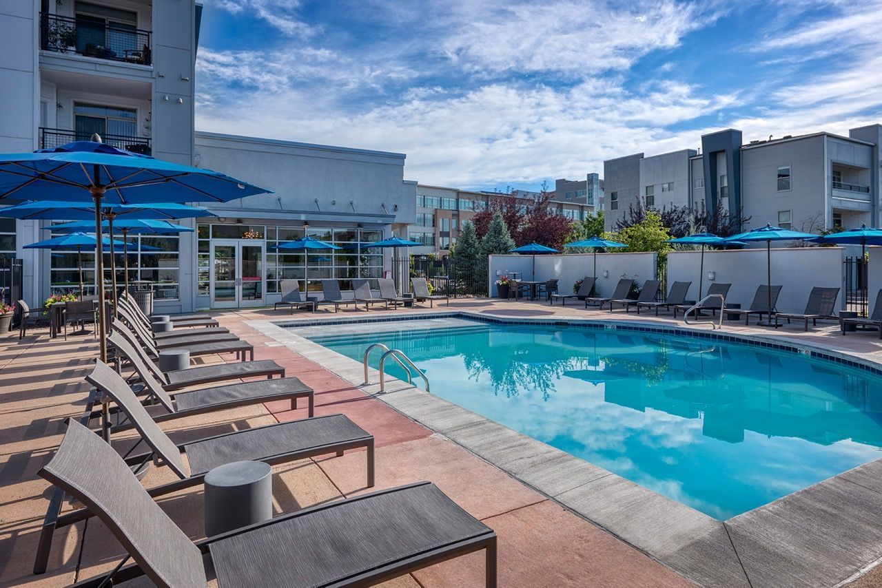 Outdoor pool area at an apartment community with lounge chairs and blue umbrellas.