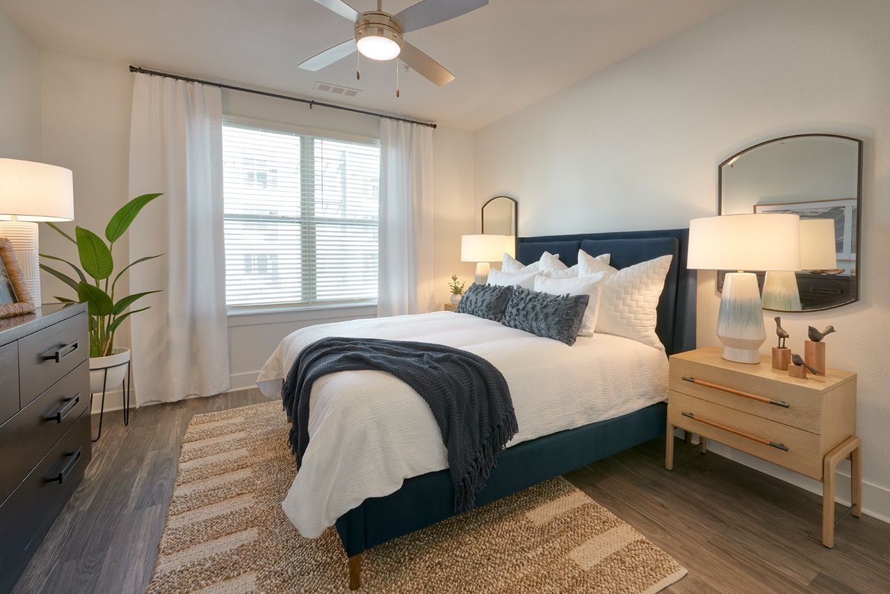 Bedroom with blue upholstered bed, white bedding, two nightstands, dresser, and a large window.