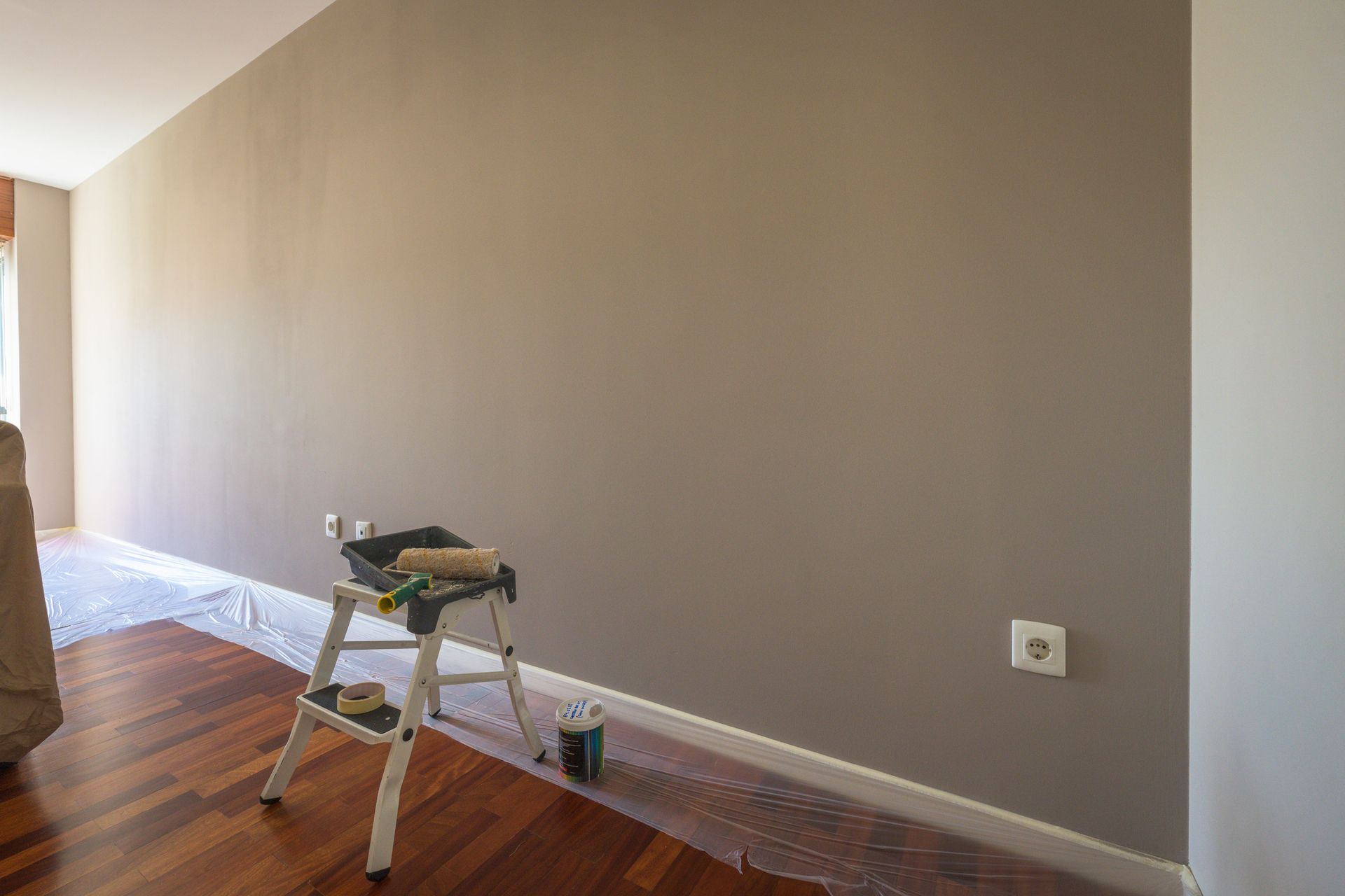 Room with a painted gray wall; painting supplies on a step stool and flooring covered in plastic.