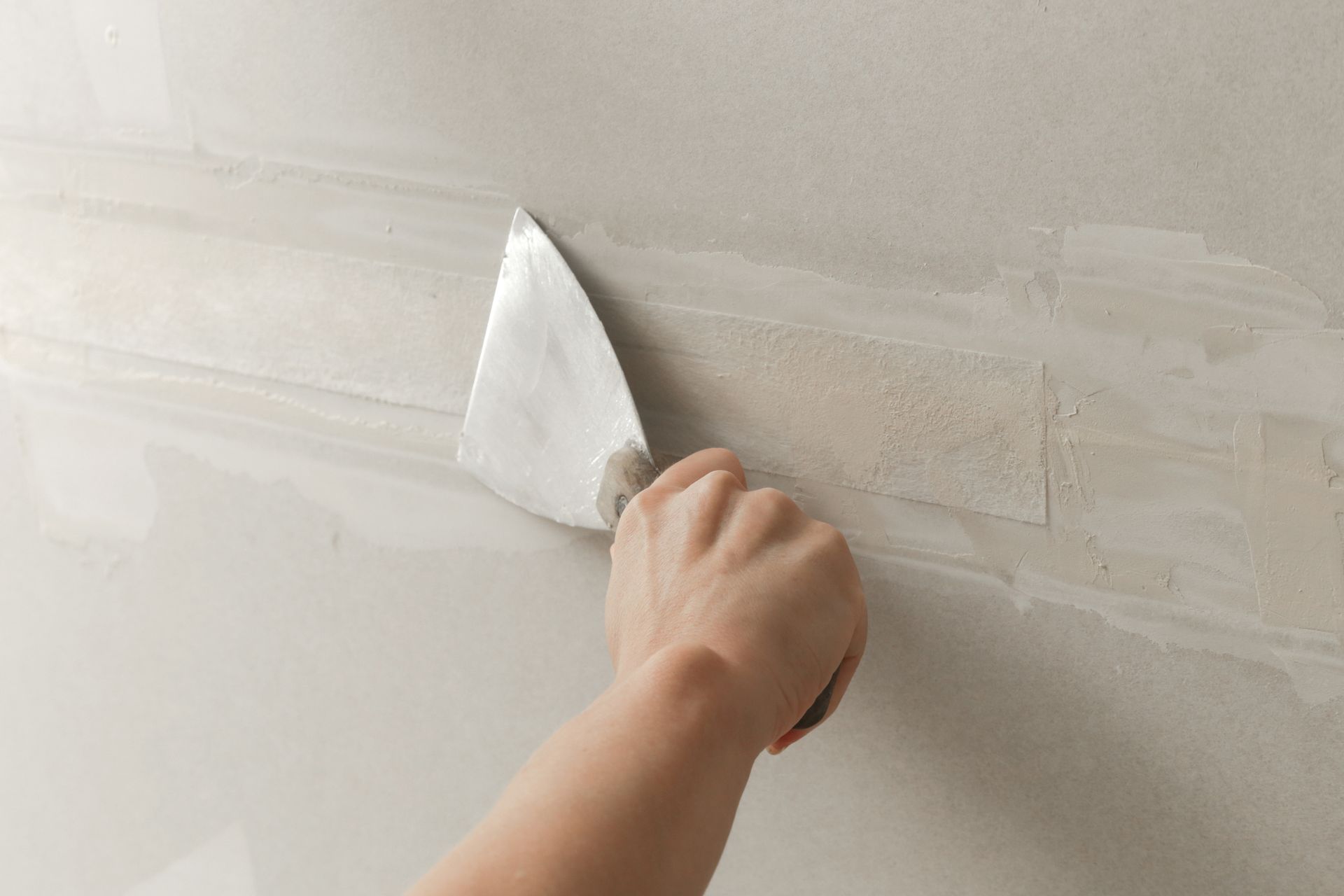 Person using a putty knife to smooth drywall joint compound on a wall.