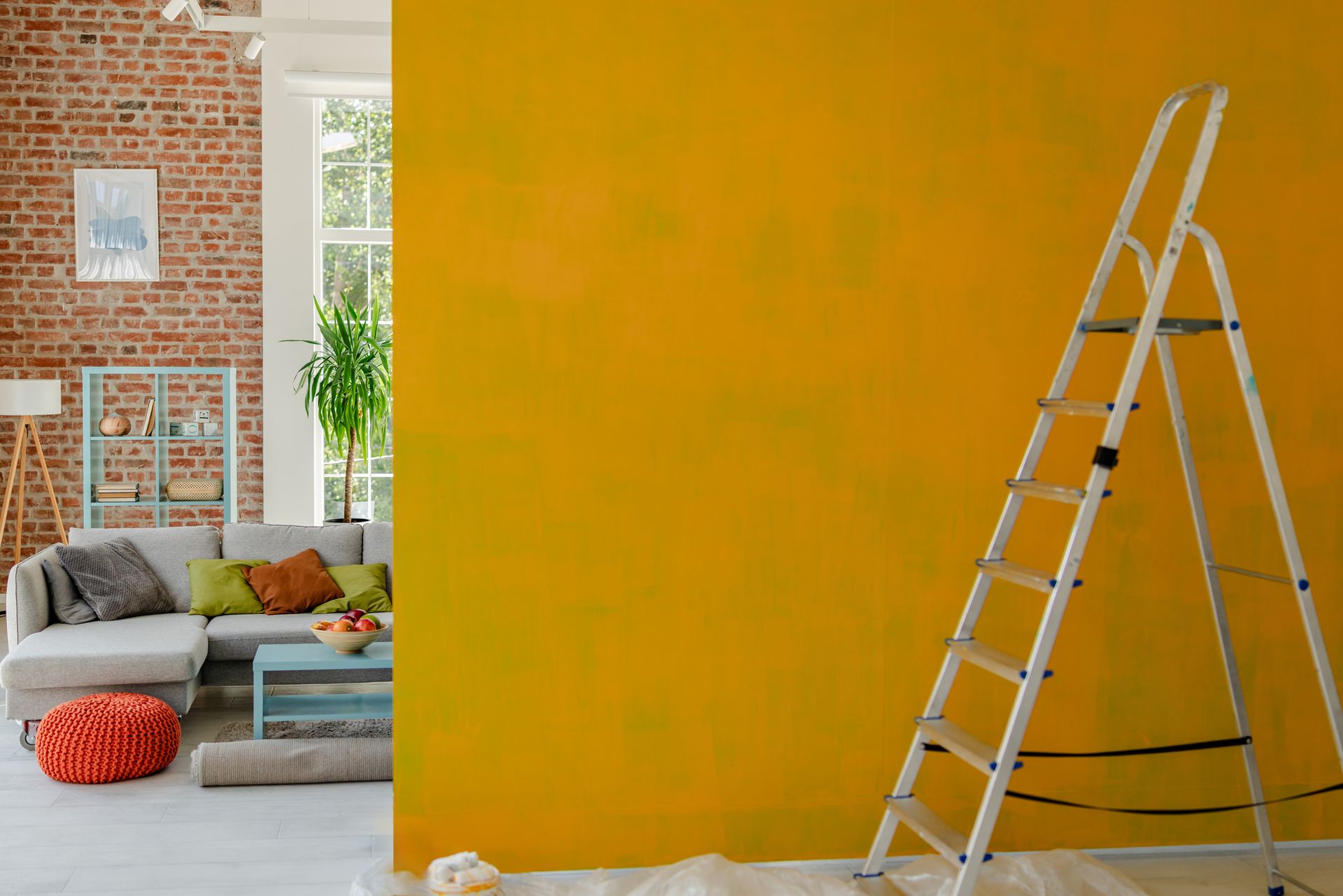 Yellow wall being painted with a ladder in front; living room in background.