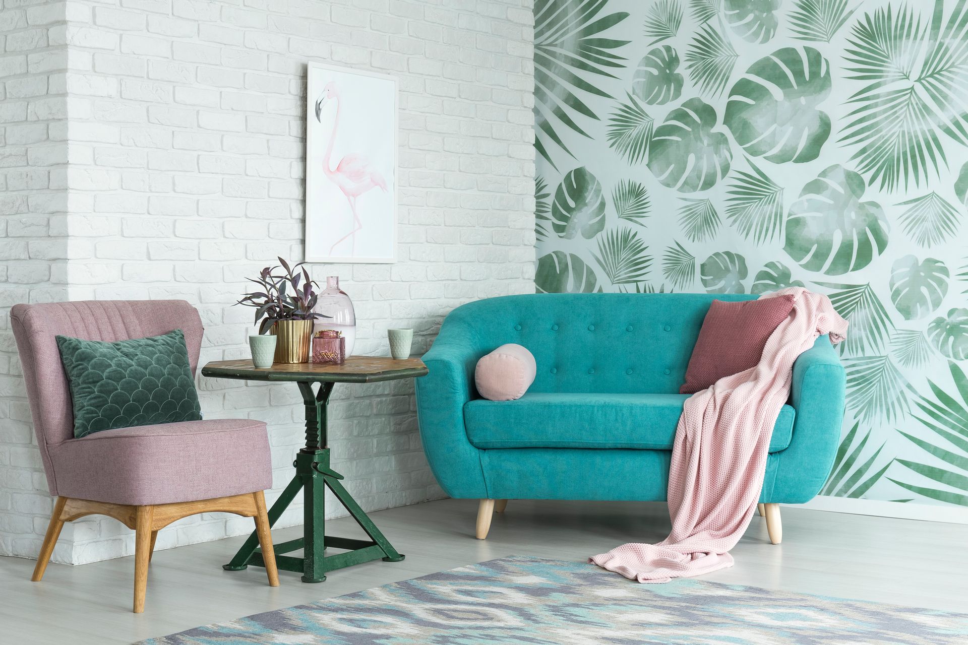 Living room with teal couch, pink chair, tropical wallpaper, small table, and pink accents.