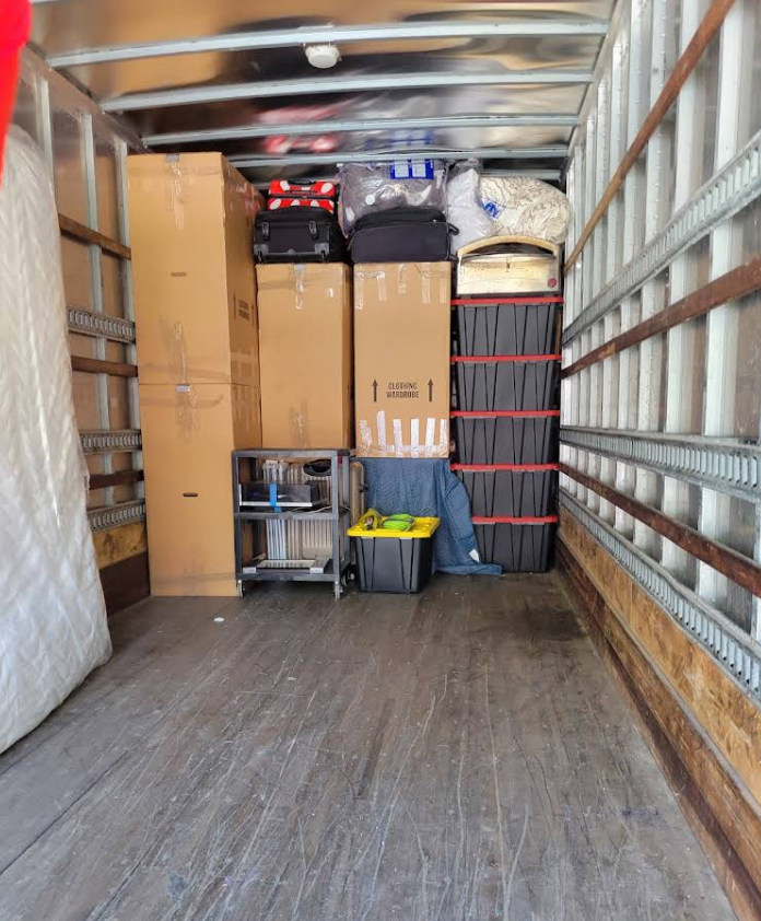 Inside a moving truck: packed boxes, luggage, mattress, and other items.