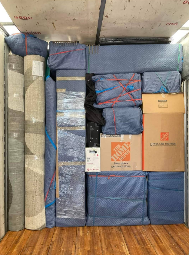 Boxes and furniture wrapped in blue blankets fill the interior of a moving truck.