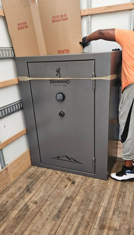 Person securing a large gray Browning gun safe in a moving truck.