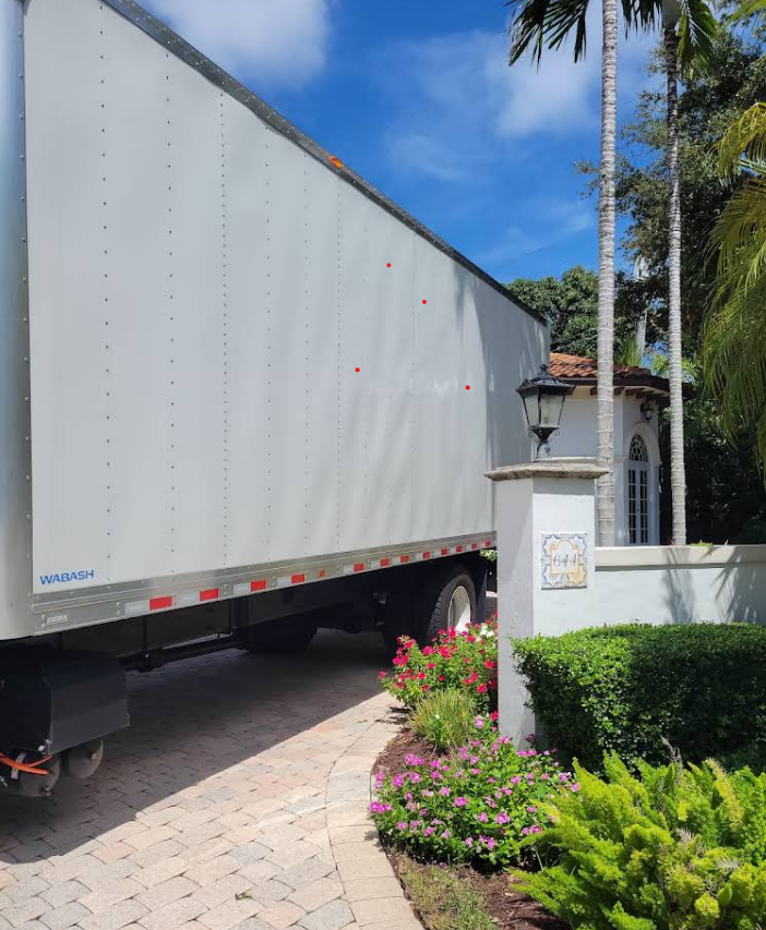 Moving truck parked in driveway of a house with a sign and greenery.