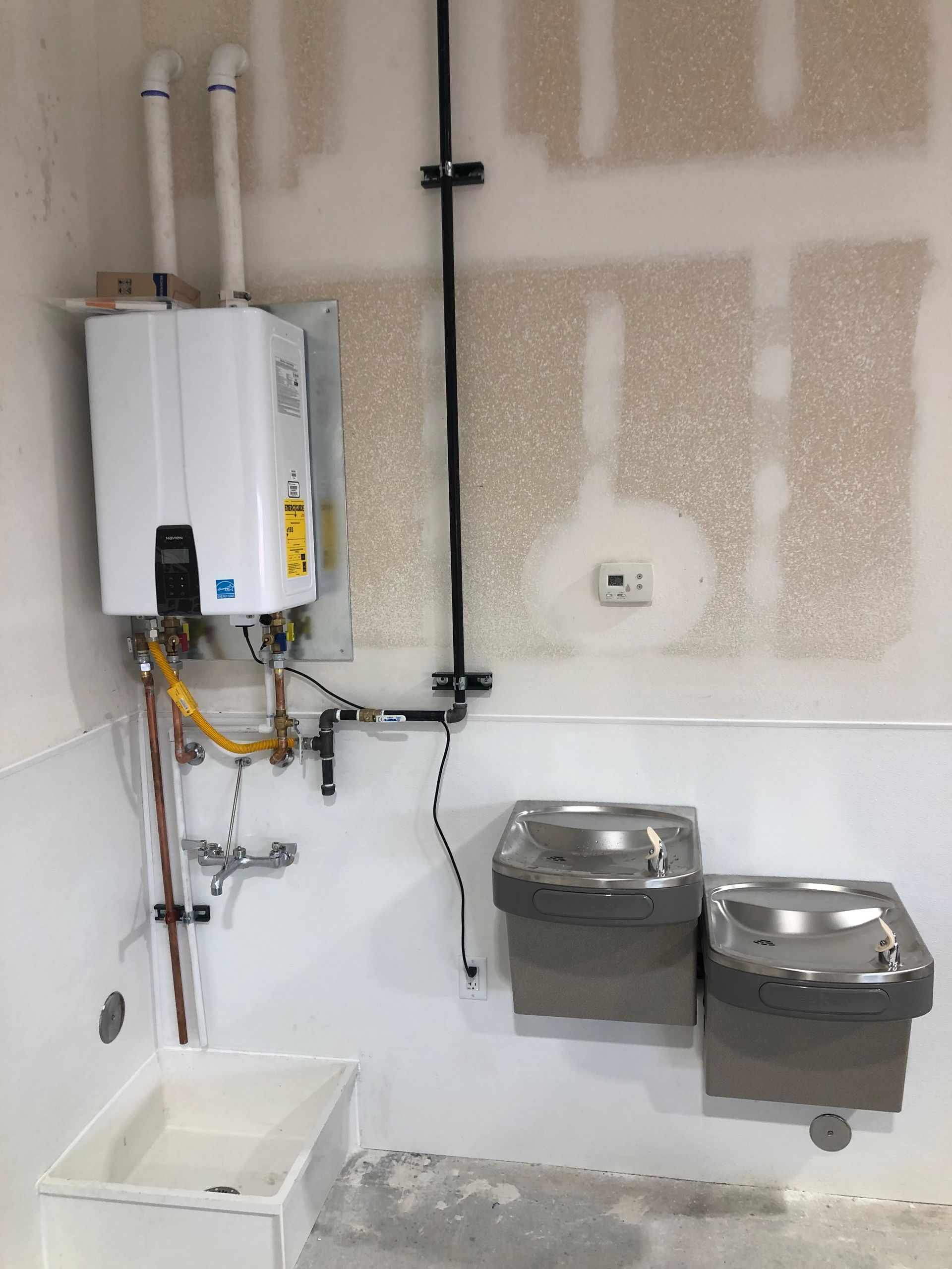 A wall-mounted water heater above a utility sink, with two water fountains to the right.