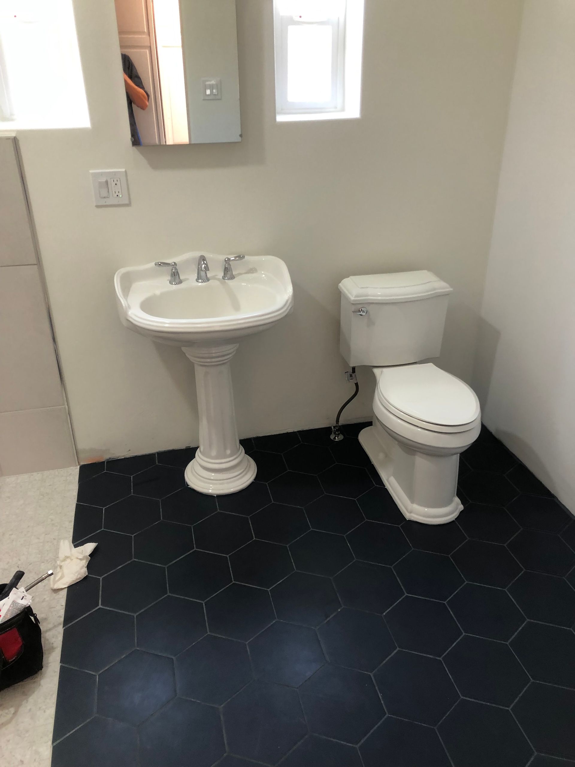 Bathroom with pedestal sink and toilet on a black hexagon tile floor, white walls.