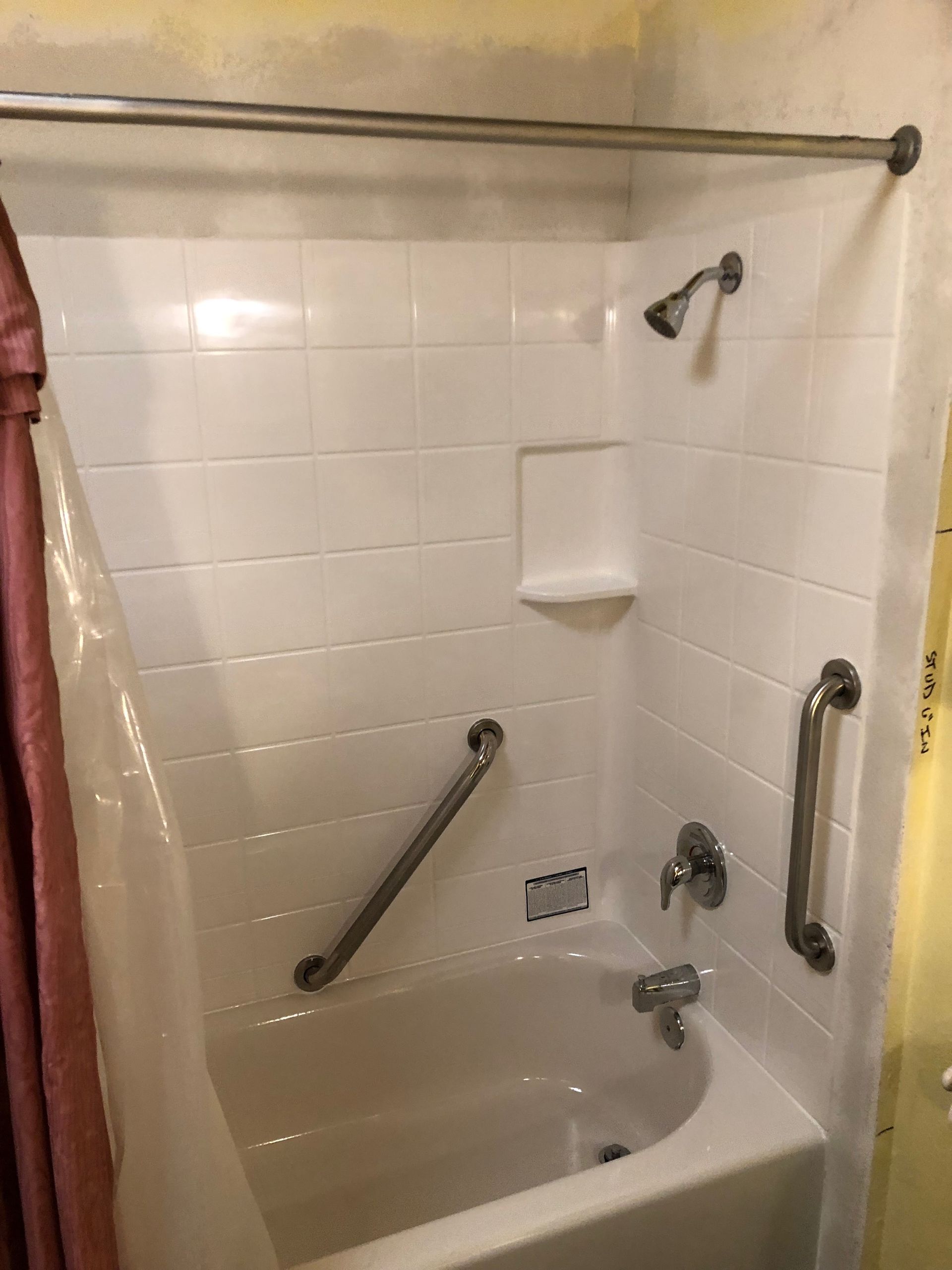 White-tiled shower with grab bars, shower head, and soap dish. A curtain hangs to the left.
