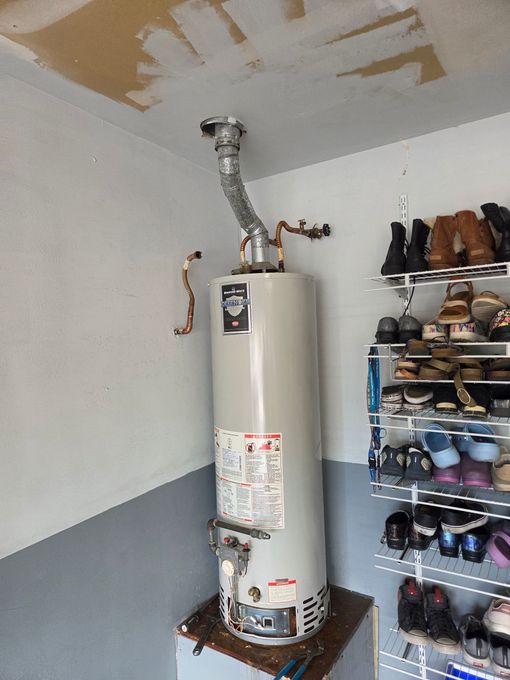 Person using a wrench to work on the top of a white water heater, with copper and plastic fittings.