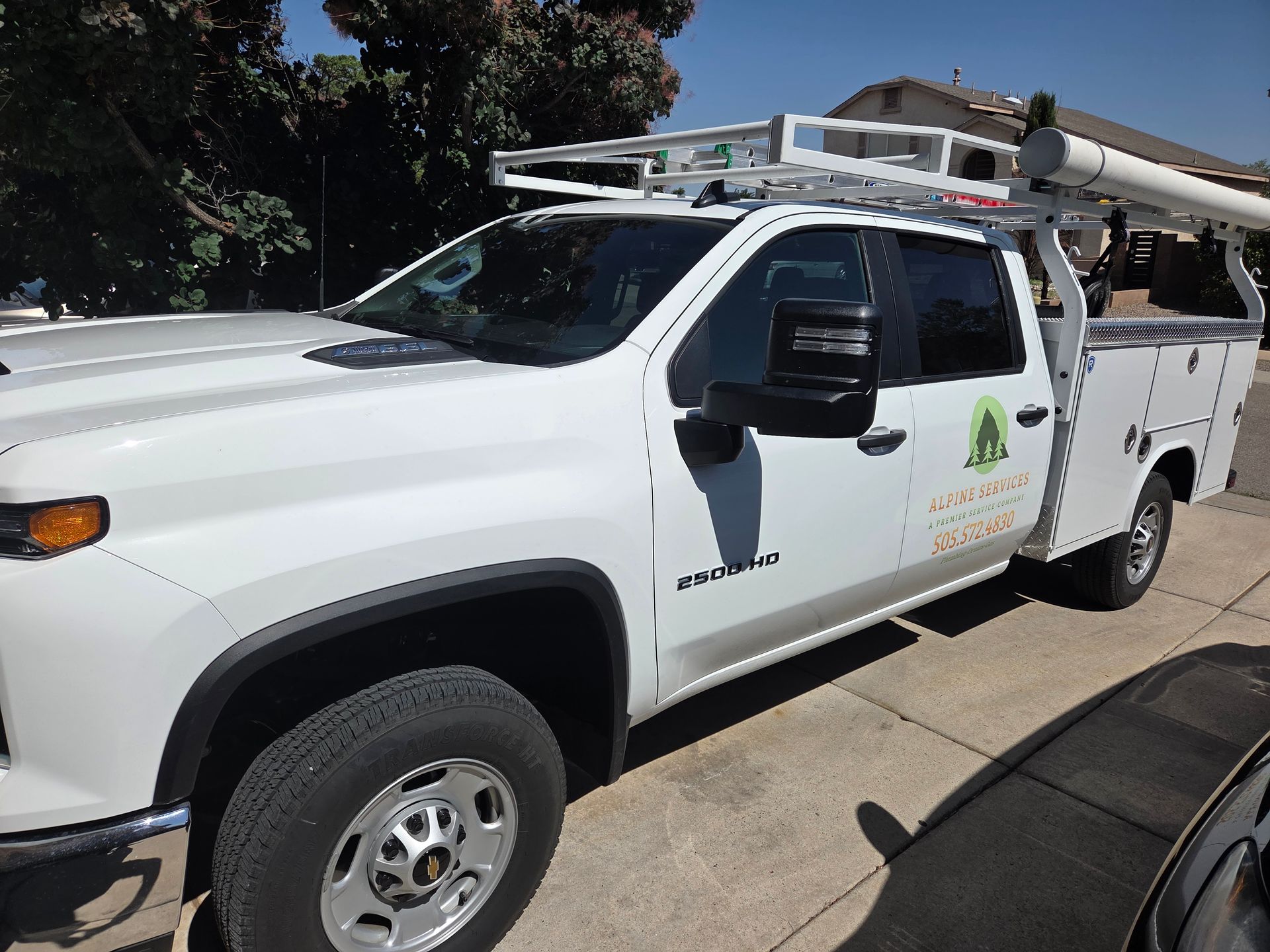 White work truck parked on a street, with a ladder rack and toolboxes.