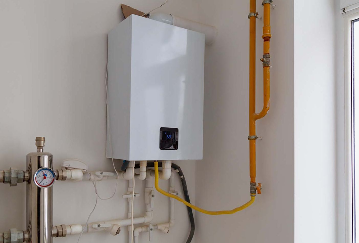 Hand using a wrench to work on a water heater, beside a blue-capped expansion tank.