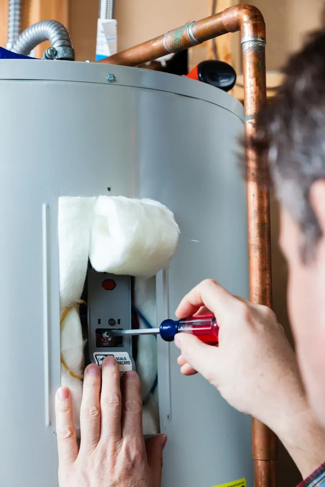 Person uses a screwdriver on a water heater control panel; indoor setting.