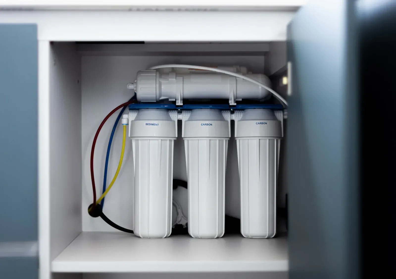 Reverse osmosis water filtration system inside a cabinet with white filters, pipes, and blue accents.