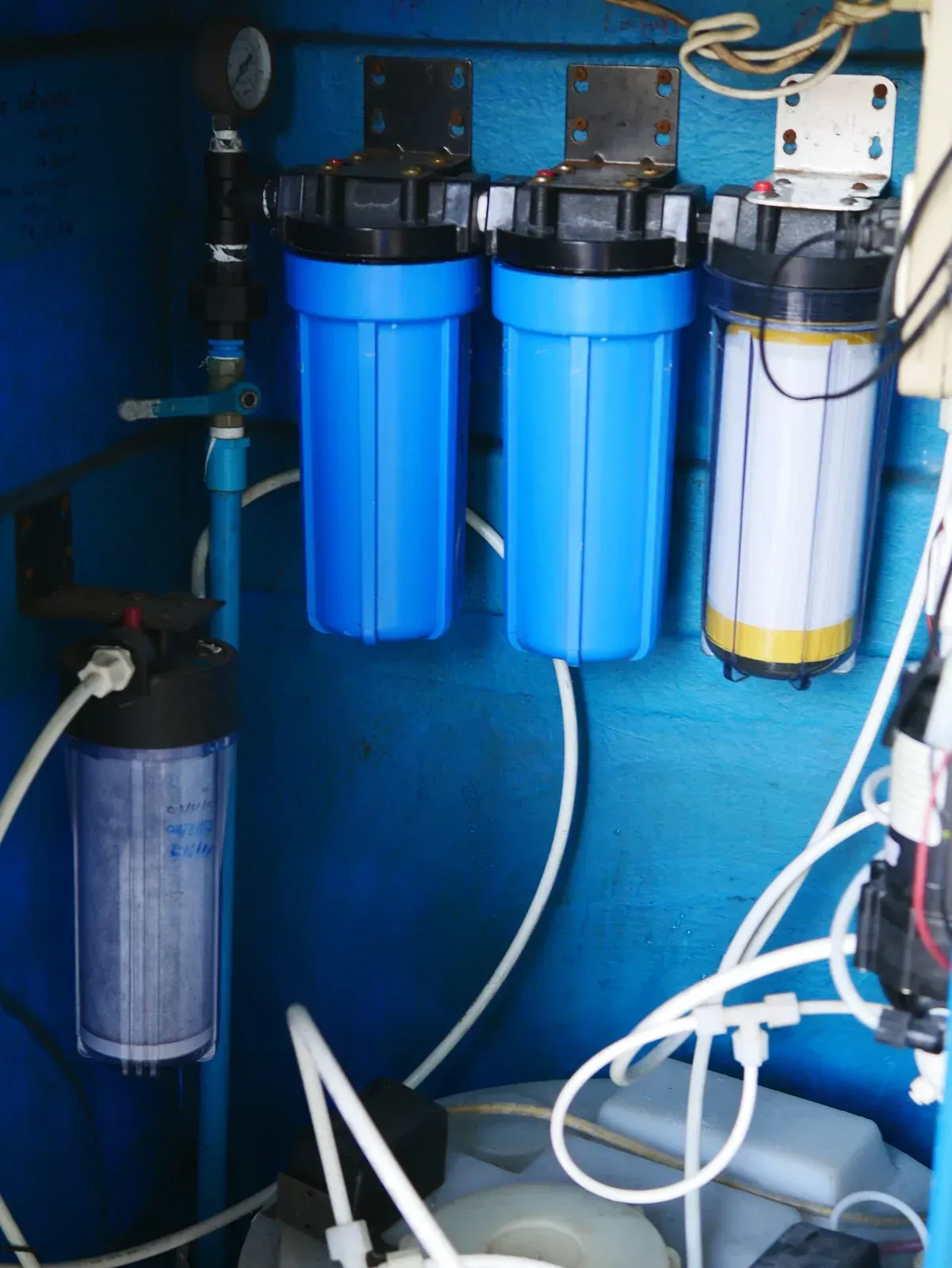 Blue water filter system with four canisters, connected by white tubing, mounted on a blue surface.