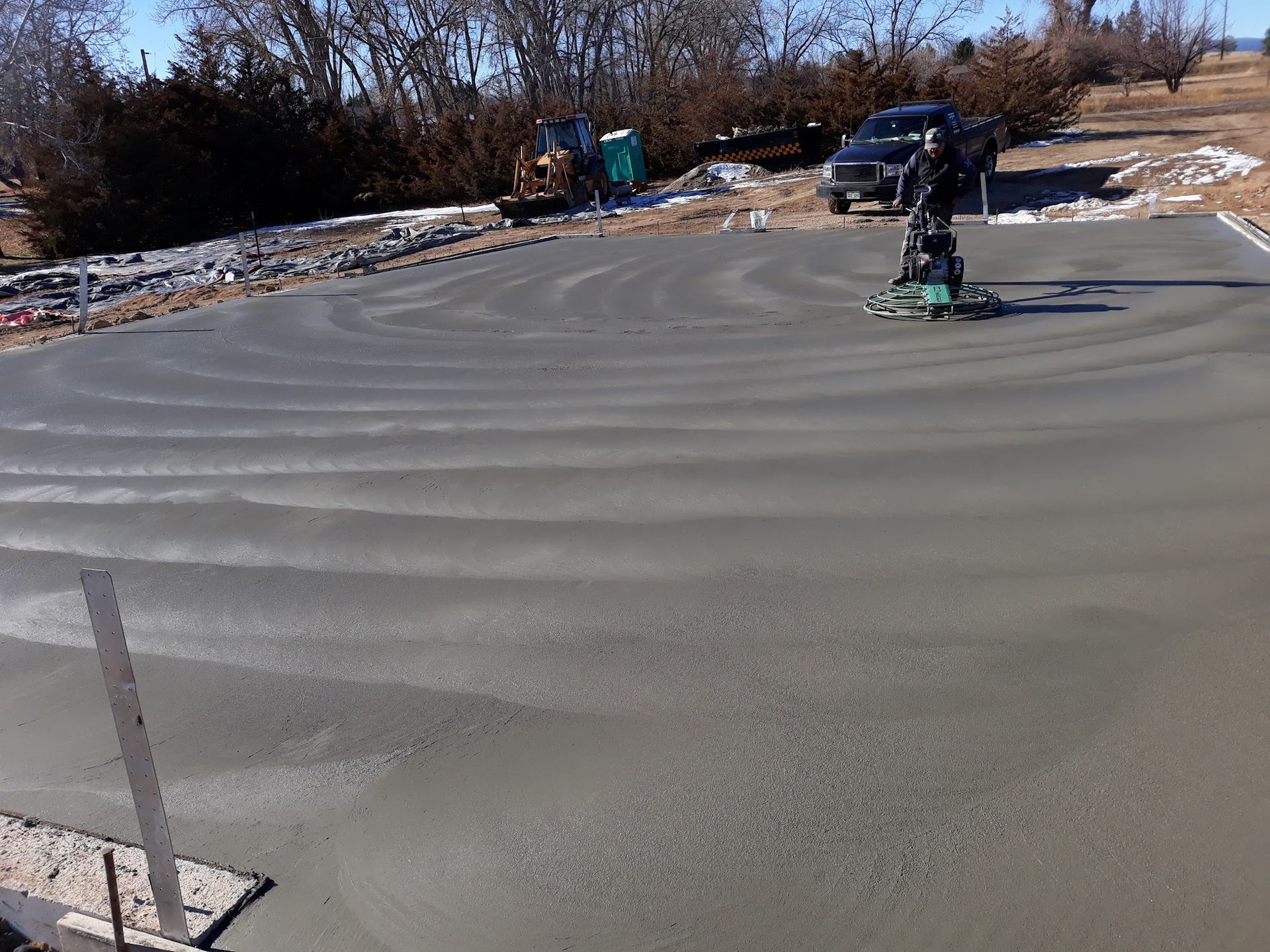 A worker smoothing wet concrete with a power trowel on a sunny day.