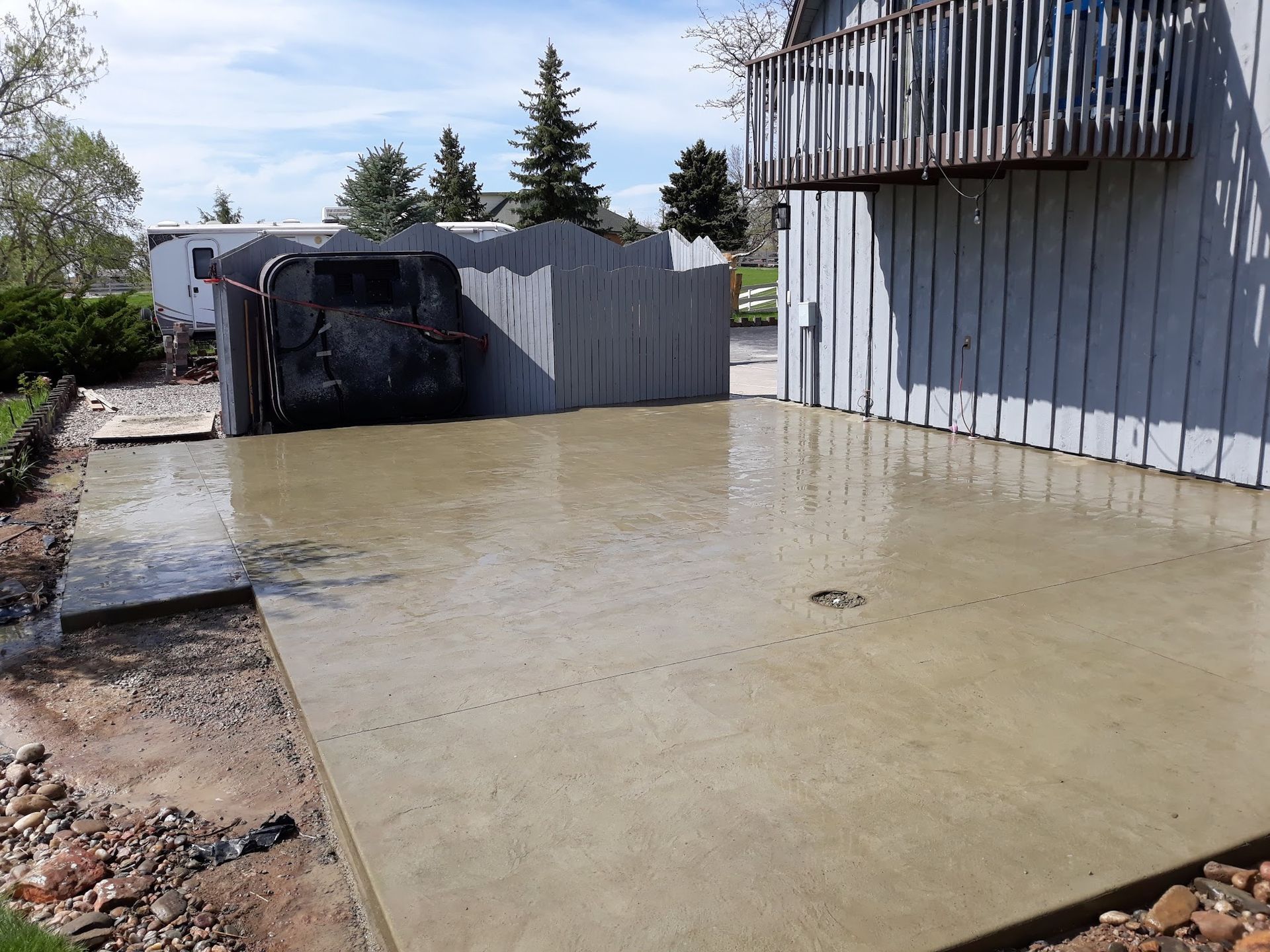 Concrete patio area next to a weathered building with a deck, some gravel, and a fence.