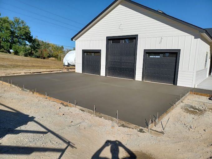 Newly poured concrete pad in front of a white building with black garage doors.