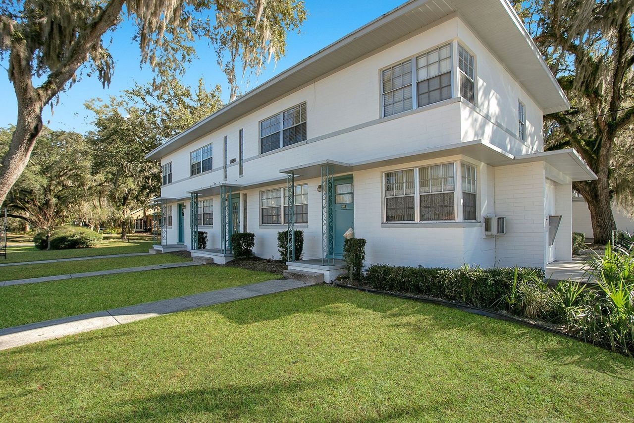 A white apartment building with blue doors and a lush green lawn.