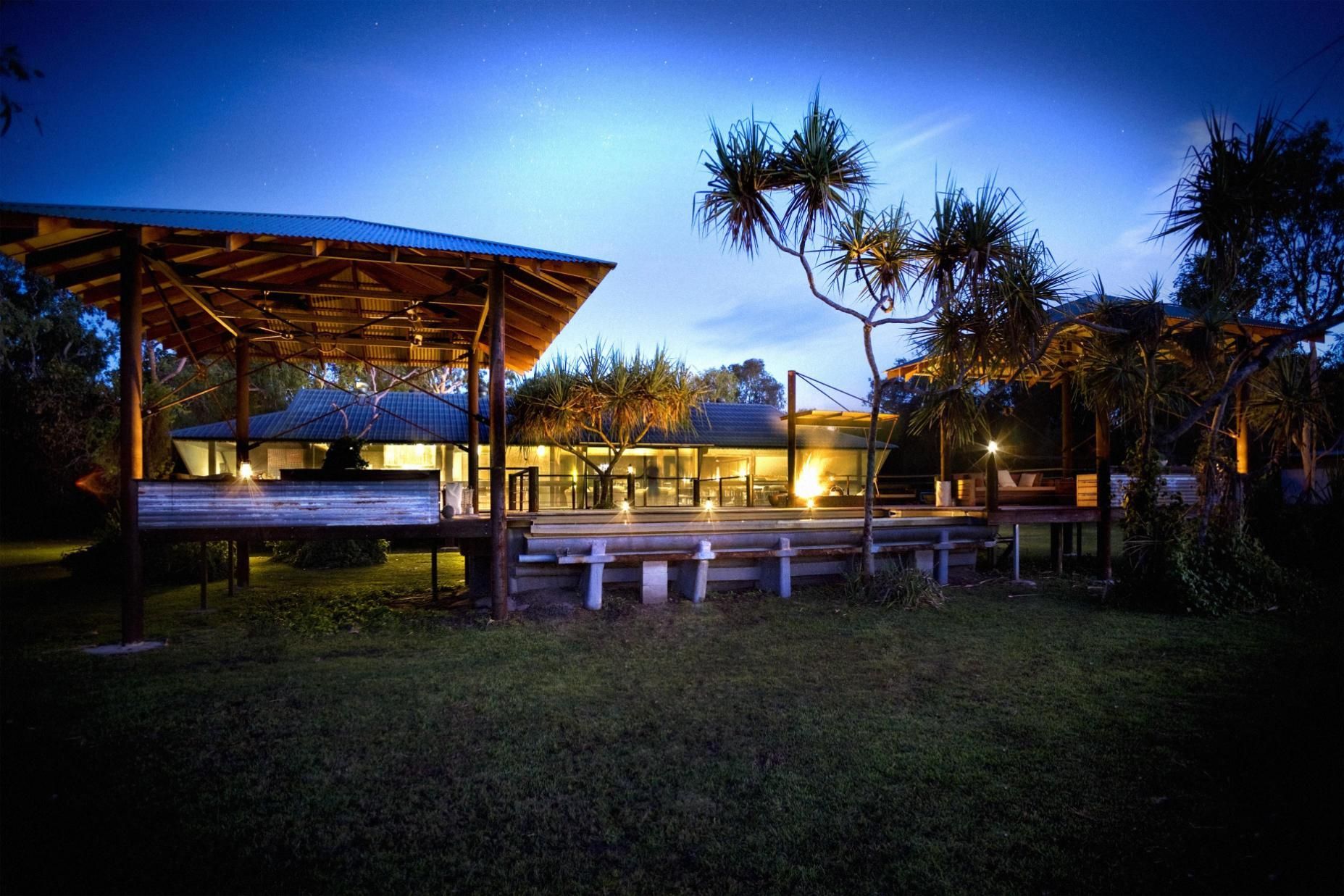 A white building with wooden privacy screens under a corrugated metal awning, surrounded by green shrubs.