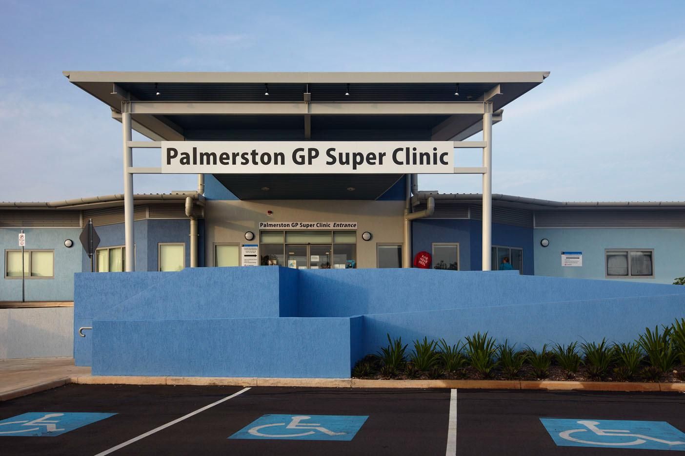 The Palmerston GP Super Clinic building with a blue facade, prominent signage, and accessible parking spaces in front.