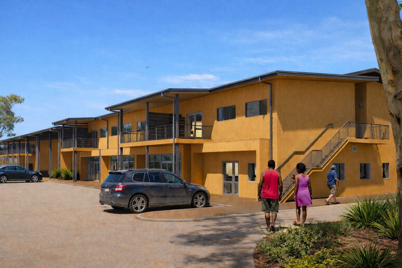 A multi-level yellow building with balconies and stairs, set under a blue sky, with people walking and a parked car nearby.