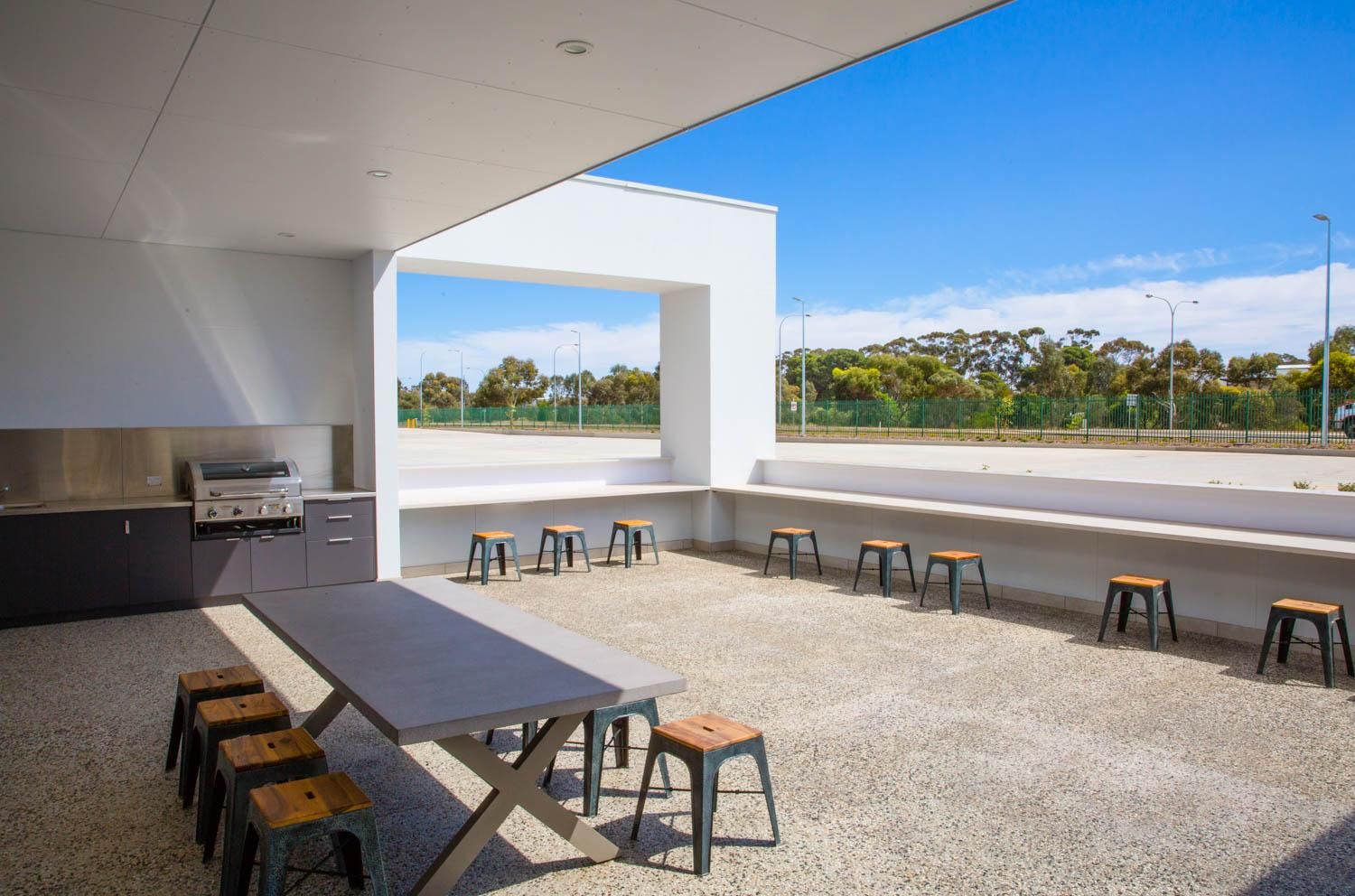 A white building with wooden privacy screens under a corrugated metal awning, surrounded by green shrubs.