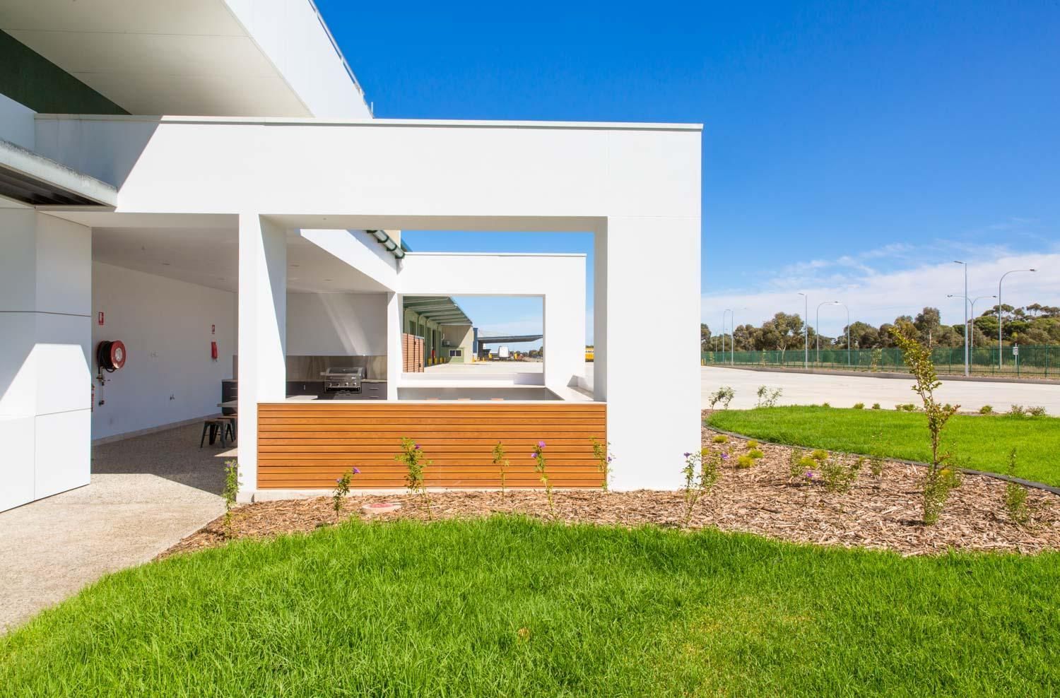 A white building with wooden privacy screens under a corrugated metal awning, surrounded by green shrubs.