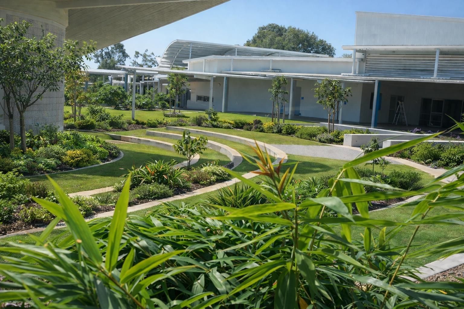A curved stone garden path winds through a bright, landscaped courtyard with lush greenery and modern white architecture.