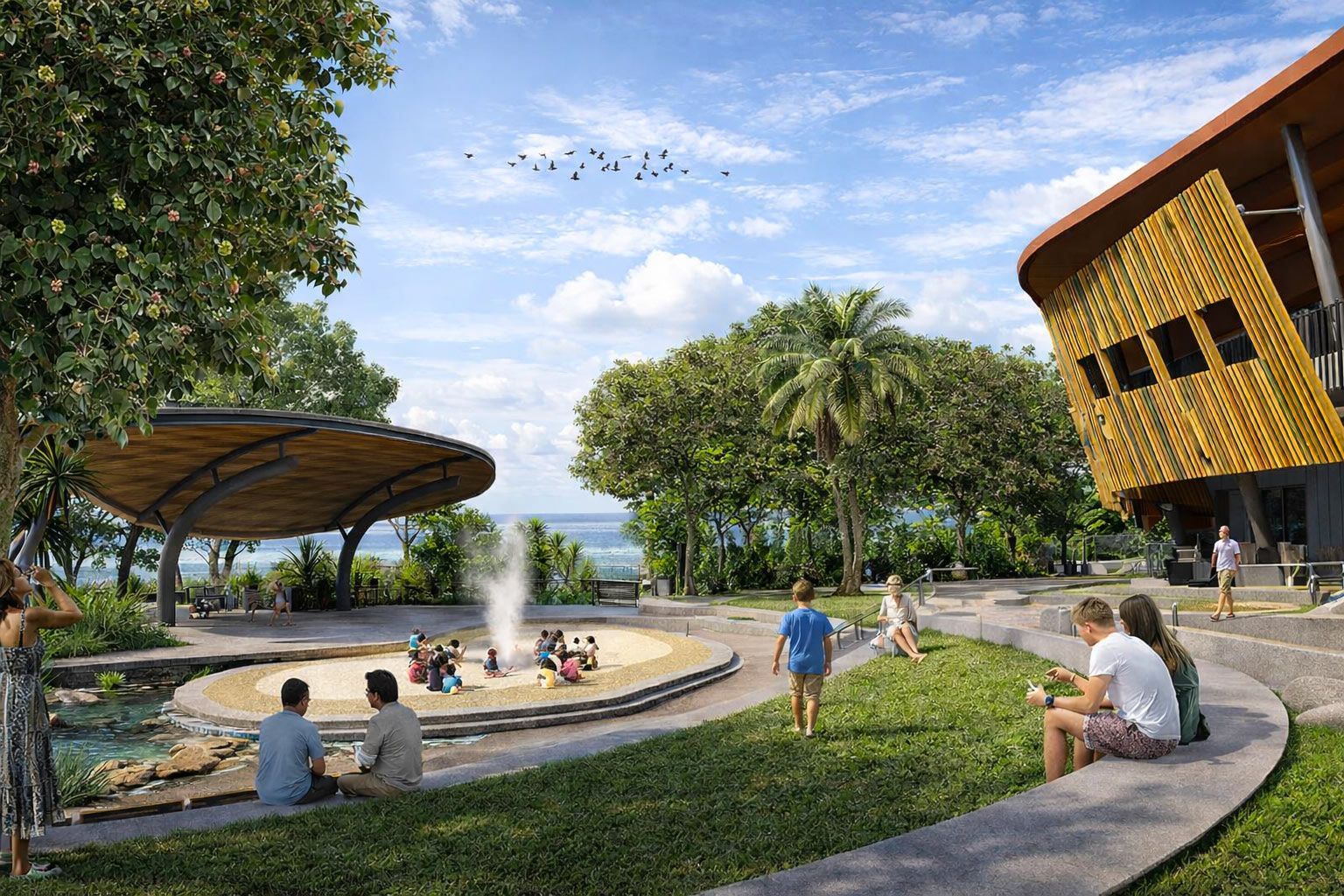 People enjoy a sunny park with a fountain, circular seating, trees, and a modern wooden building under a blue sky.