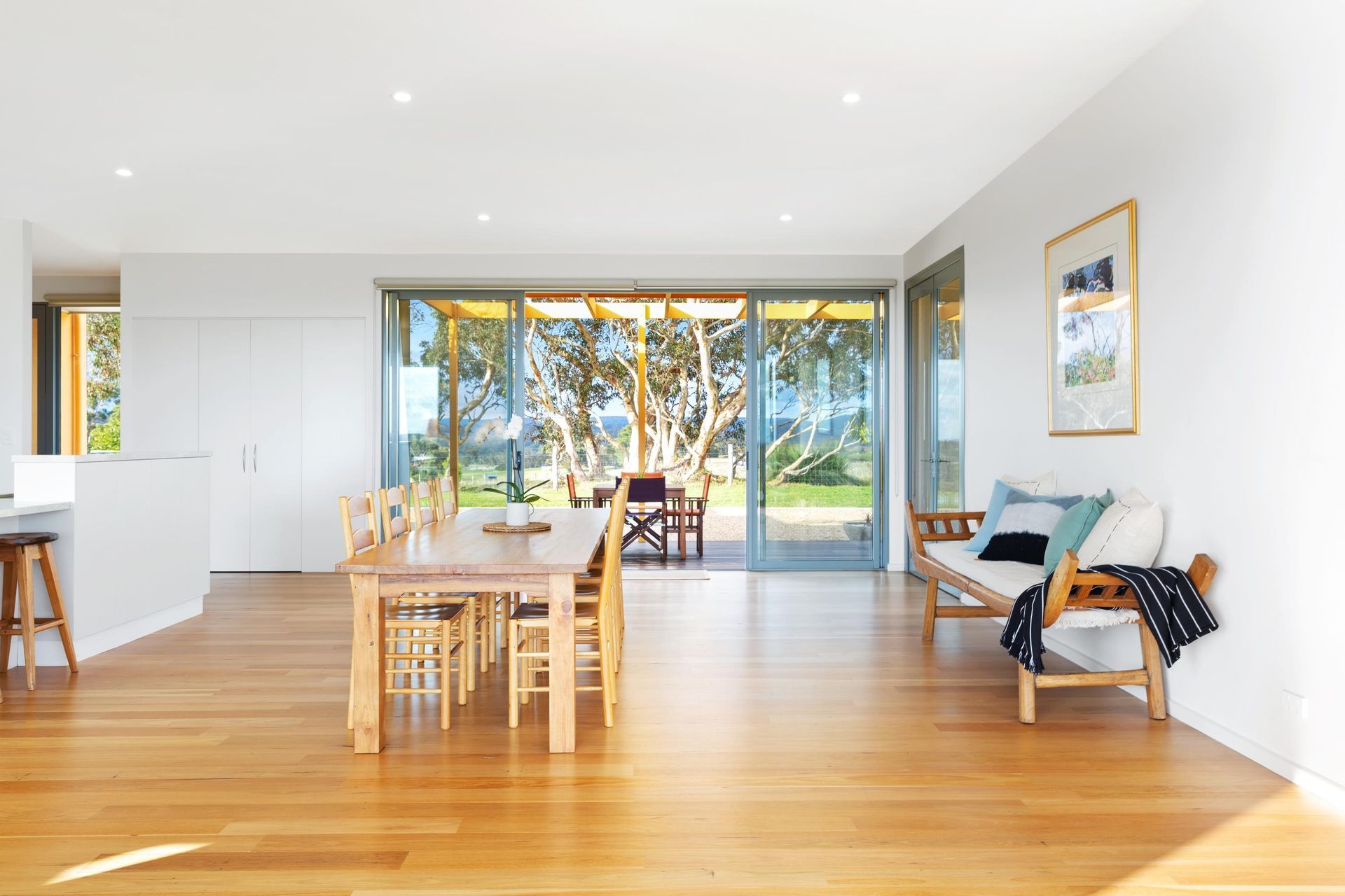 A shaded walkway with white trellis structures covered in vines, leading to a street with a pedestrian crossing.