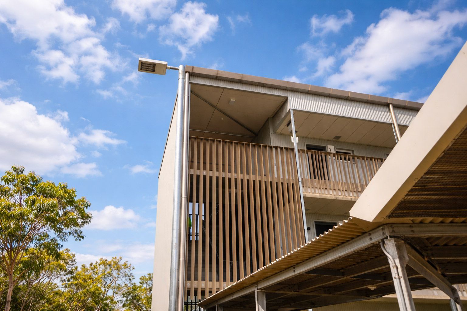A multi-story building featuring wooden vertical slats on the exterior, set against a bright blue sky with scattered clouds.