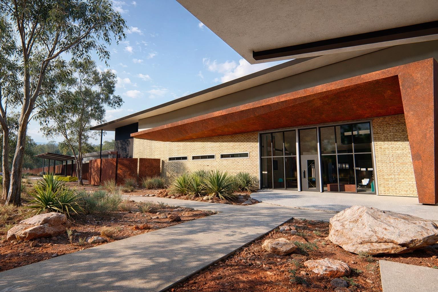 Modern school building with a large covered patio, colorful exterior walls, and native grasses in the foreground.