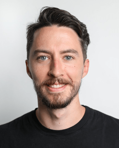 A man with a beard is wearing a black shirt and smiling for the camera.